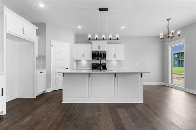 kitchen with dark wood finished floors, stainless steel microwave, white cabinets, a sink, and a kitchen island with sink