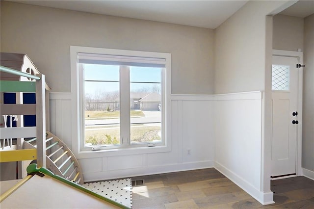 interior space with a wainscoted wall, a decorative wall, visible vents, and wood finished floors