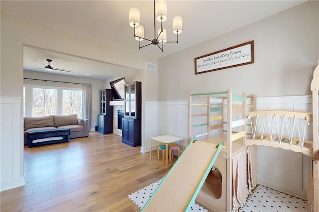 bedroom featuring a decorative wall, wainscoting, light wood-type flooring, and an inviting chandelier