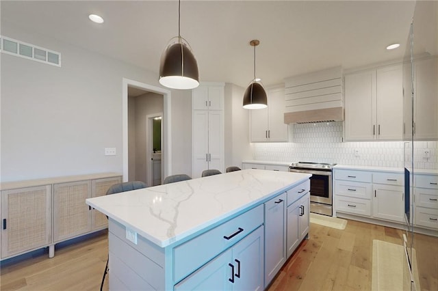 kitchen featuring light wood finished floors, visible vents, backsplash, a center island, and stainless steel range with electric stovetop