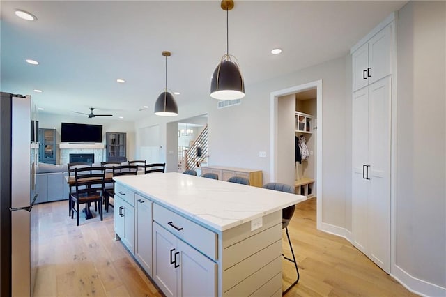 kitchen with a kitchen island, a breakfast bar area, light wood-style flooring, freestanding refrigerator, and a ceiling fan