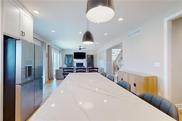 kitchen featuring visible vents, stainless steel refrigerator with ice dispenser, open floor plan, white cabinets, and hanging light fixtures