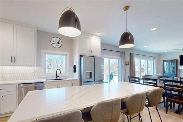 kitchen with a sink, a kitchen breakfast bar, open floor plan, white cabinetry, and stainless steel appliances