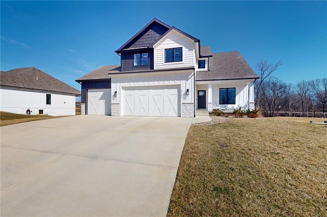 view of front of house featuring board and batten siding, concrete driveway, a front yard, stone siding, and an attached garage