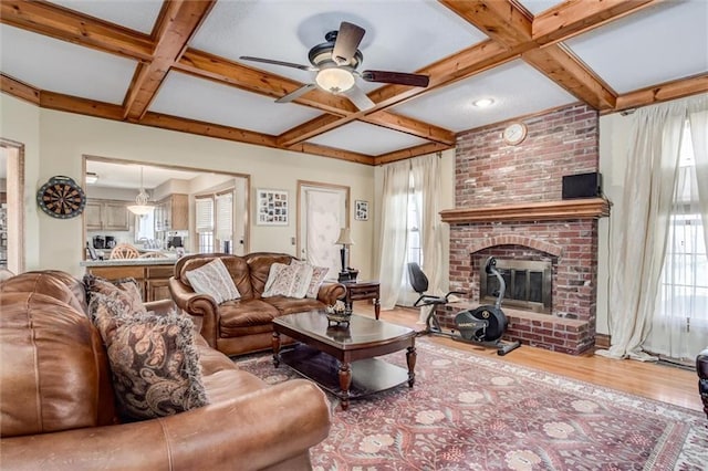 living area featuring a healthy amount of sunlight, a brick fireplace, wood finished floors, coffered ceiling, and a ceiling fan