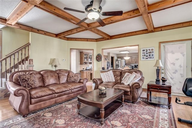 living room featuring ceiling fan, stairway, beamed ceiling, wood finished floors, and coffered ceiling