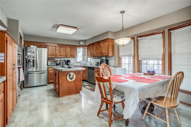 kitchen with pendant lighting, a center island, appliances with stainless steel finishes, brown cabinetry, and light countertops