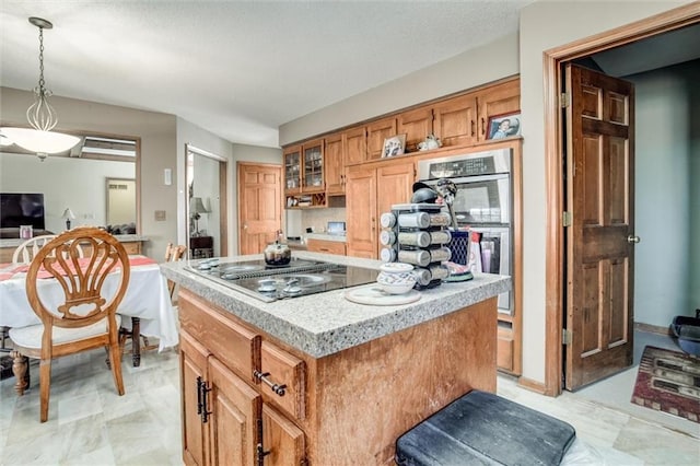 kitchen with a kitchen island, light countertops, glass insert cabinets, pendant lighting, and black electric stovetop