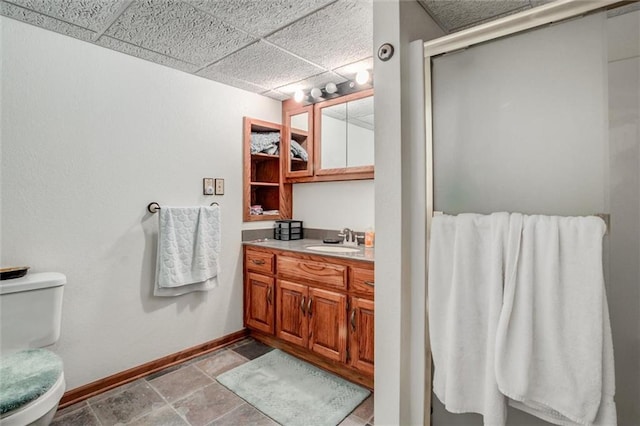 full bathroom featuring toilet, a stall shower, a drop ceiling, baseboards, and vanity