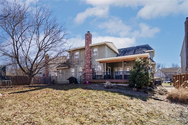 back of house featuring a lawn, a chimney, a trampoline, and fence