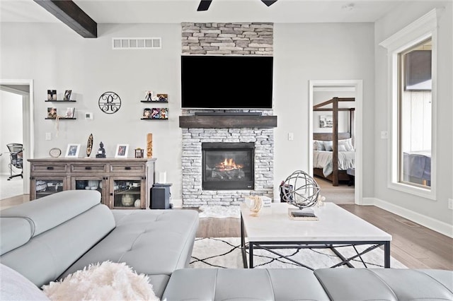 living room with visible vents, ceiling fan, wood finished floors, beamed ceiling, and a fireplace