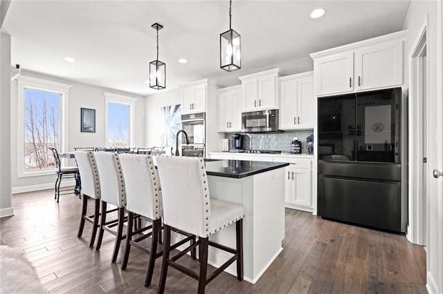 kitchen featuring tasteful backsplash, stainless steel microwave, a breakfast bar area, black refrigerator, and a kitchen island with sink