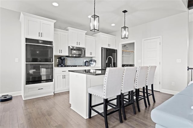 kitchen with dobule oven black, fridge, decorative backsplash, stainless steel microwave, and a center island with sink