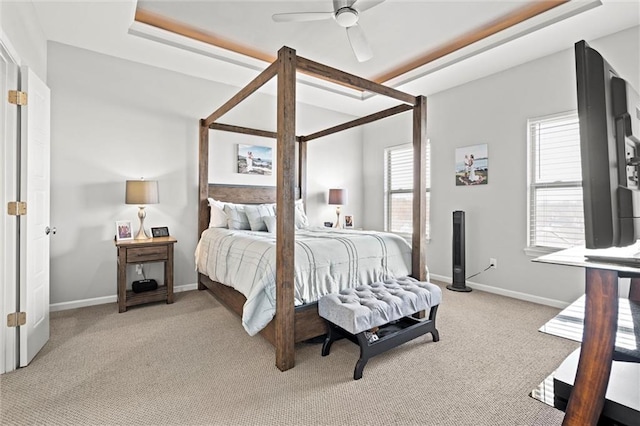 bedroom featuring a raised ceiling, light colored carpet, ceiling fan, and baseboards