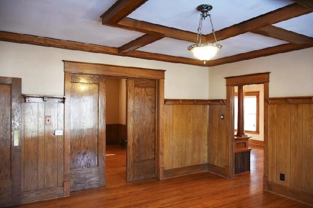 empty room with beam ceiling, wood finished floors, and wainscoting