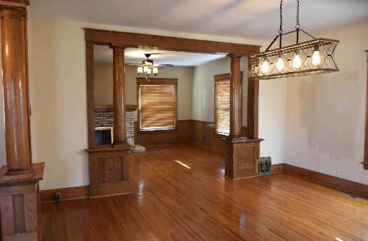 unfurnished dining area with a wainscoted wall, wood finished floors, wood walls, and ornate columns