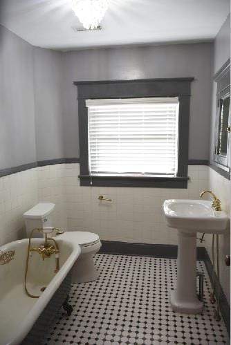 bathroom featuring tile patterned floors, a wainscoted wall, a soaking tub, and toilet