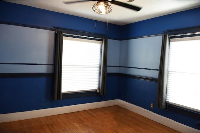 unfurnished room with baseboards, plenty of natural light, wood finished floors, and a ceiling fan