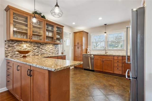 kitchen with light stone countertops, a peninsula, a sink, stainless steel appliances, and brown cabinets