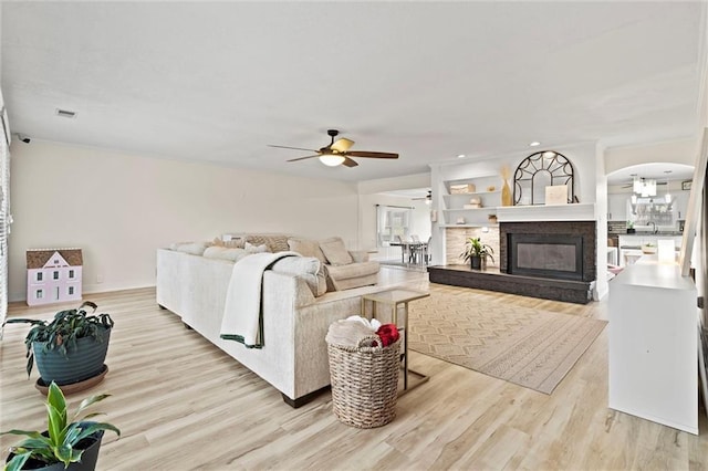 living room with a glass covered fireplace, wood finished floors, arched walkways, and ceiling fan