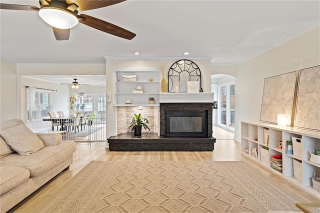 living area featuring wood finished floors, a ceiling fan, arched walkways, ornamental molding, and a glass covered fireplace