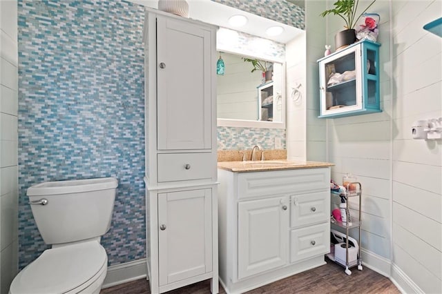 bathroom with baseboards, toilet, vanity, wood finished floors, and tile walls