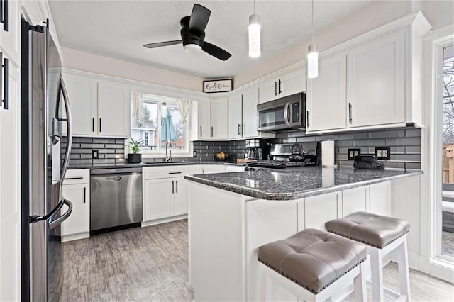 kitchen featuring pendant lighting, a sink, appliances with stainless steel finishes, a peninsula, and white cabinets