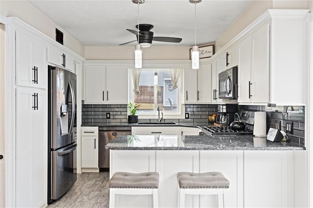 kitchen featuring white cabinetry, a peninsula, stainless steel appliances, and a sink