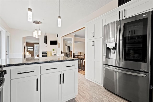 kitchen with light wood finished floors, dark stone counters, arched walkways, white cabinets, and stainless steel refrigerator with ice dispenser