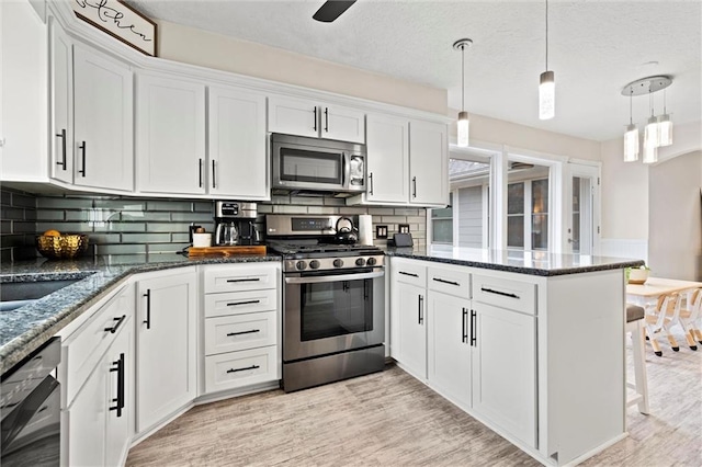 kitchen featuring light wood finished floors, white cabinets, appliances with stainless steel finishes, and a peninsula