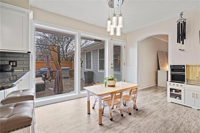 dining space featuring an inviting chandelier, light wood-style flooring, arched walkways, and a textured ceiling