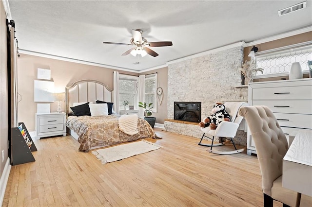 bedroom featuring visible vents, a ceiling fan, wood finished floors, a fireplace, and crown molding