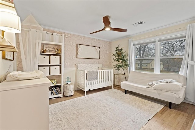 bedroom featuring wallpapered walls, wood finished floors, visible vents, and ornamental molding