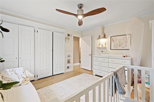 bedroom featuring light wood finished floors, visible vents, multiple closets, and ornamental molding