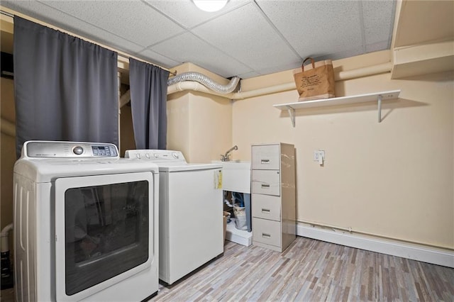 clothes washing area with light wood finished floors, a sink, a baseboard radiator, and separate washer and dryer