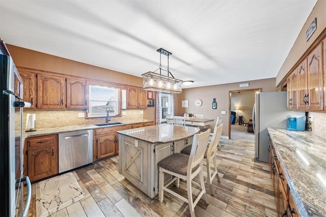 kitchen with a kitchen island, a sink, light wood-style floors, appliances with stainless steel finishes, and backsplash