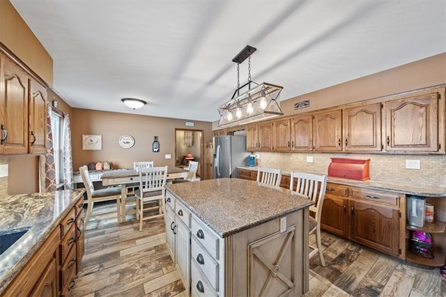 kitchen featuring light stone counters, backsplash, stainless steel refrigerator with ice dispenser, and light wood finished floors