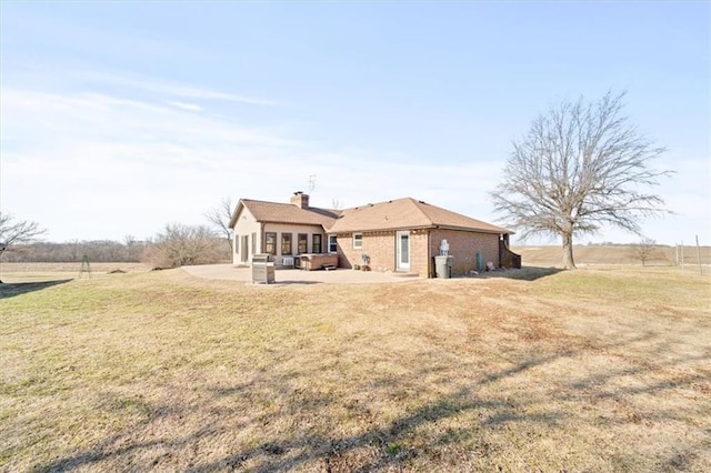 rear view of property featuring a patio, a yard, brick siding, and a chimney