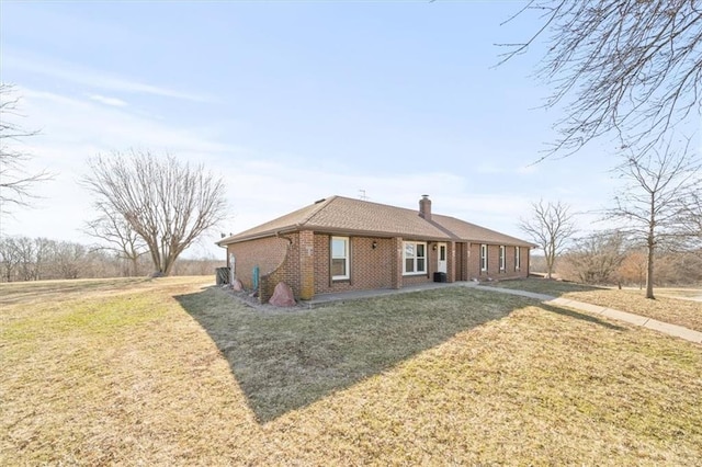 rear view of property featuring brick siding, a chimney, and a yard