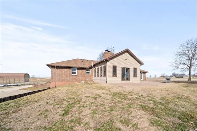 back of property with brick siding, a patio area, a lawn, and a chimney