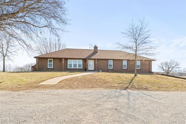 single story home featuring brick siding, a chimney, and a front yard