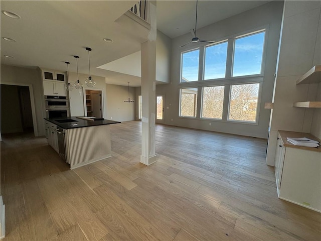 kitchen featuring open floor plan, white cabinetry, double oven, light wood finished floors, and a towering ceiling