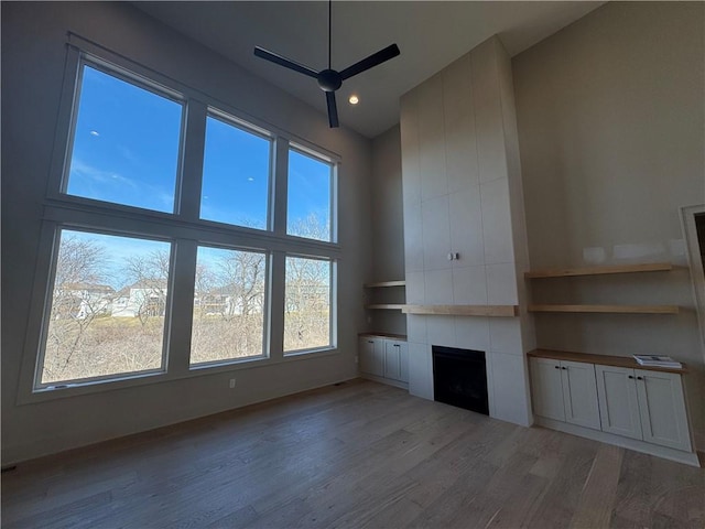 unfurnished living room featuring light wood finished floors, a tile fireplace, a high ceiling, and a ceiling fan