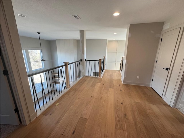 corridor with light wood finished floors, visible vents, baseboards, an upstairs landing, and recessed lighting