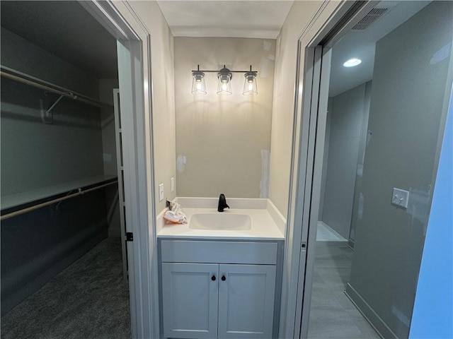 bathroom featuring vanity, a walk in closet, baseboards, and visible vents