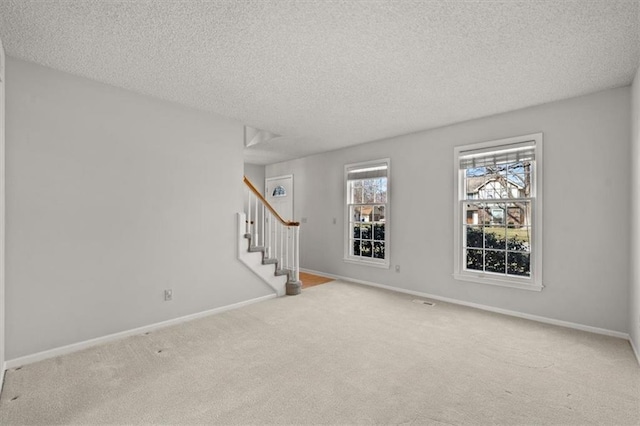 unfurnished room featuring stairway, carpet floors, a textured ceiling, and baseboards