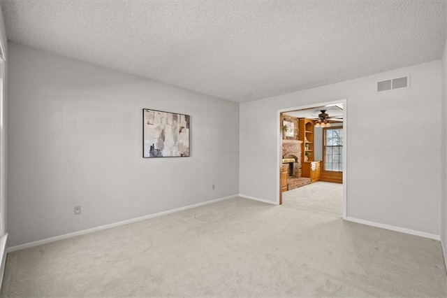 spare room featuring a textured ceiling, a fireplace, visible vents, and light carpet