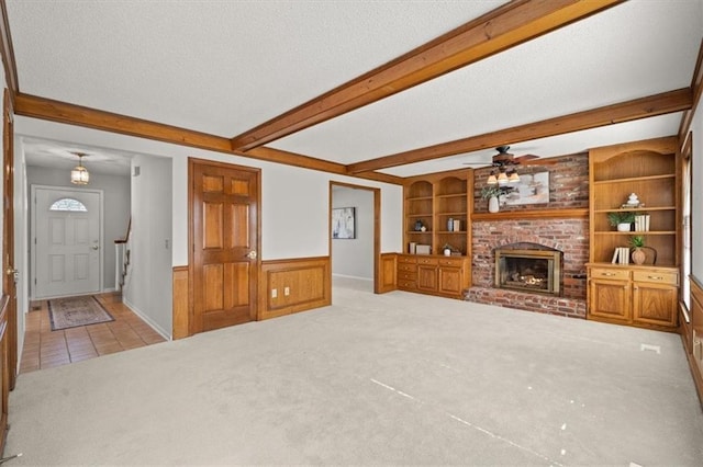 carpeted living area featuring beamed ceiling, built in shelves, a wainscoted wall, a textured ceiling, and a fireplace