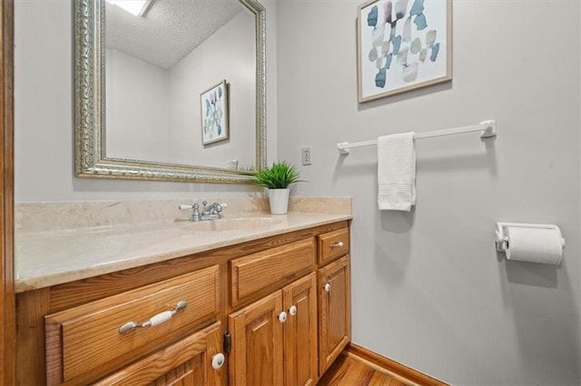 bathroom with baseboards, a textured ceiling, wood finished floors, and vanity