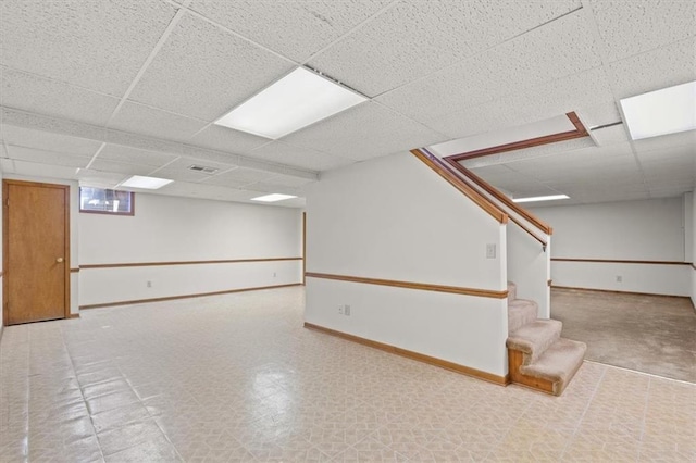 basement featuring tile patterned floors, a paneled ceiling, baseboards, and stairs